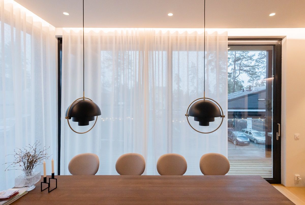 The dining area is illuminated by LED strip lighting behind light daylight curtains, flush-mounted spotlights on the ceiling and two pendant lights on the table.